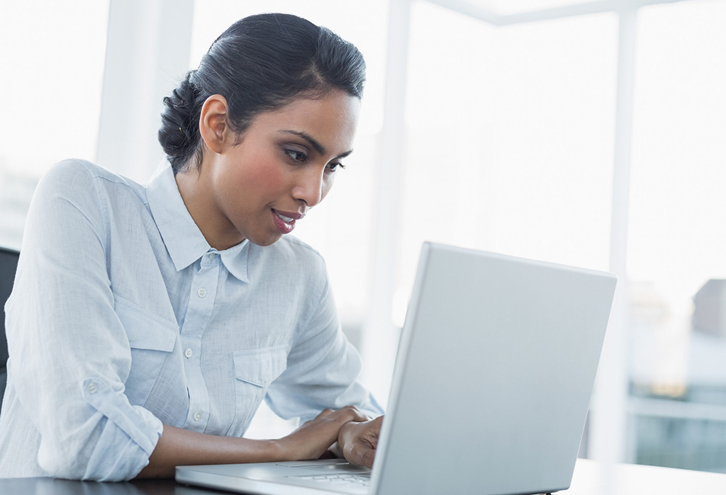 attractive young businesswoman working using her laptop sitting at her desk