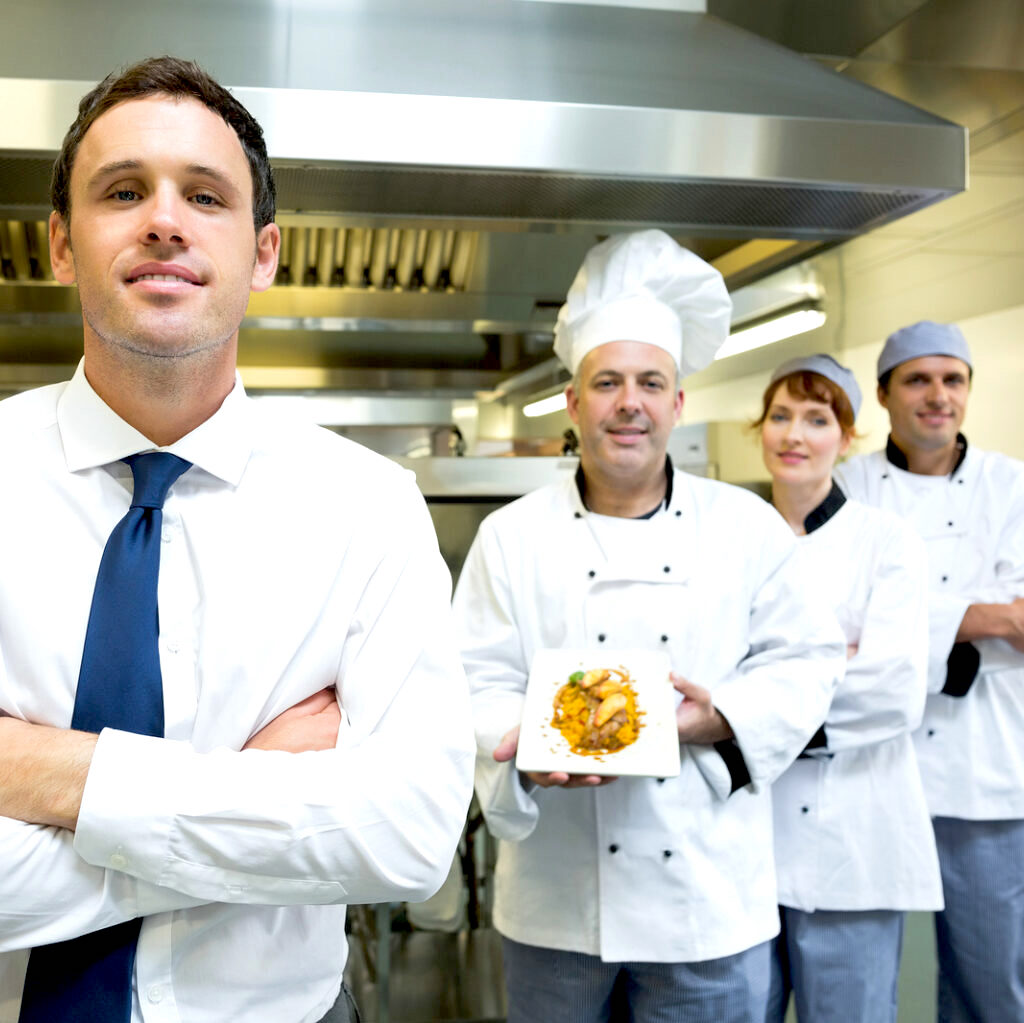 young restaurant manager posing in front of team of chefs smiling at camera